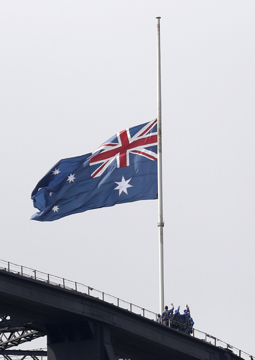 People climbing the Sydney Harbour Bridge stop under a flag flying at half-mast as mark of mourning and respect in Sydney Friday, Jan 24, 2020, for three US crew members of an aerial water tanker that crashed Thursday while battling wildfires in Australia. Photo: AP