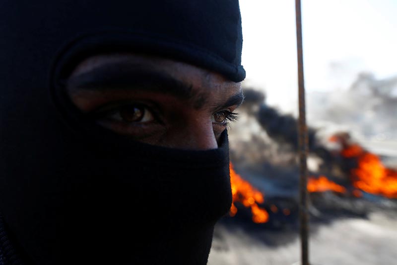 An Iraqi demonstrator covers his face near burning tires blocking a road during ongoing anti-government protests in Najaf, Iraq January 26, 2020. Photo: Reuters