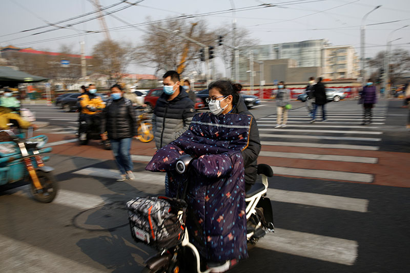 People wearing face masks ride their scooters and  walk on a street following an outbreak of the coronavirus disease (COVID-19), in Beijing, China March 30, 2020. Photo: Reuters