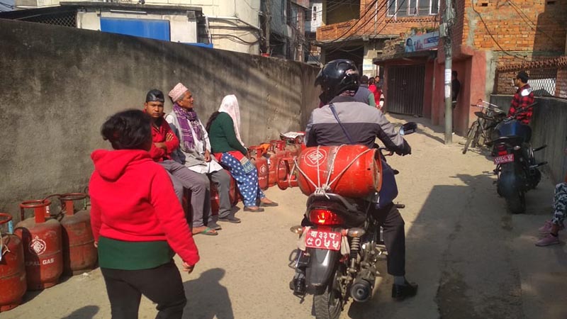 A motorcycle rider carries an LPG gas cylinder as other consumers wait in a queue to purchase the cooking gas at a retail store in Anamnagar, Kathmandu, on Friday, March 6, 2020. Photo: Suresh Chaudhary/THT