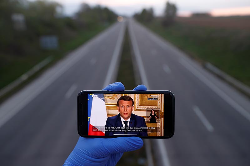 A mobile phone showing French President Emmanuel Macron, as he addresses the nation about the coronavirus disease (COVID-19) outbreak, is displayed for a photo in front of an almost empty motorway in Strasbourg, France, April 13, 2020. Photo: Reuters