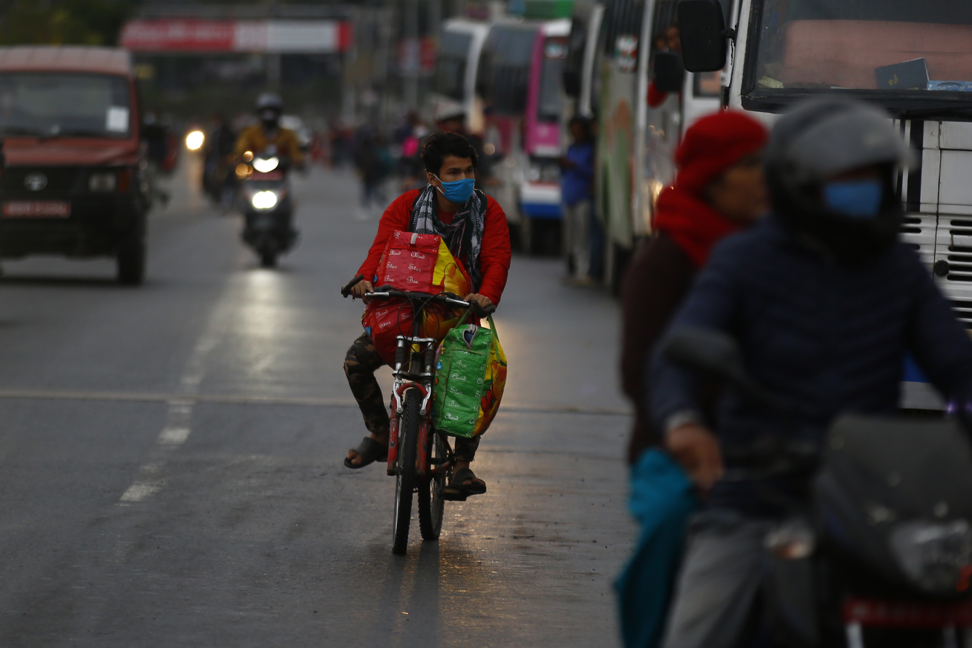 A man is seen riding his bicycle where people are waiting to board buses to return to their native villages, in Kathmandu, on Tuesday, April 21, 2020. Photo: Skanda Gautam/THT