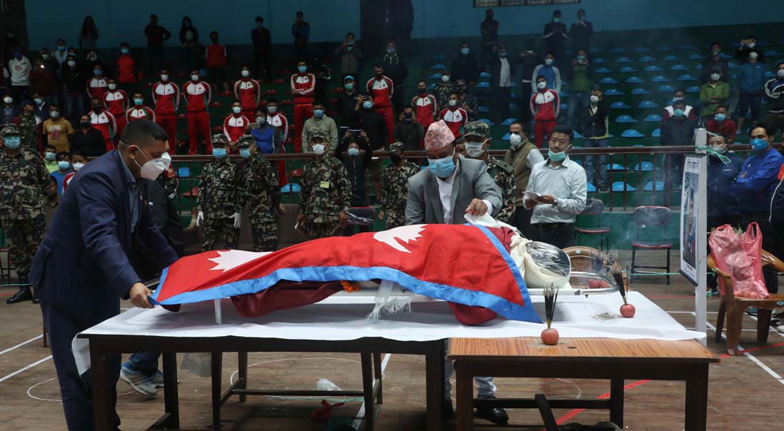Minister for Youth and Sports Jagat Bahadur Sunar and Vice-president of National Sports Council Pitamber Timsina (left) draping the national flag over the body of wushu player Birman Waiba at the NSC covered hall in Kathmandu on Monday. Photo Courtesy: NSC