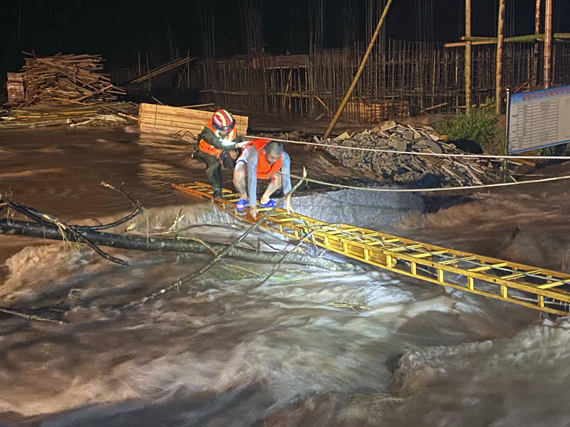A rescuer helps a worker cross a ladder to get across floodwaters from a construction site in Jing'an county in central China's Jiangxi province midnight Friday, July 3, 2020. A wide swath of southern China braced Sunday for more seasonal rains and flooding. Photo: Chinatopix via AP