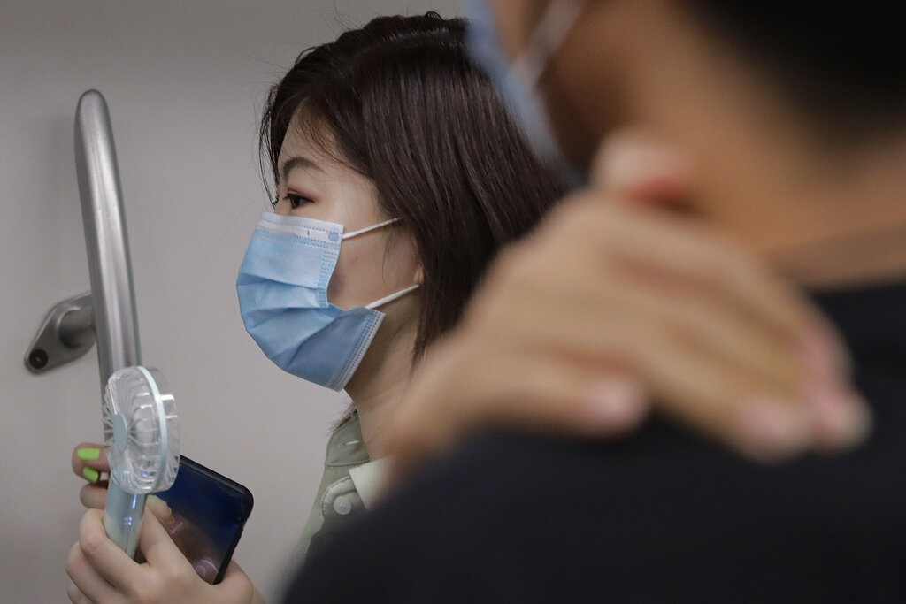 A woman wearing a face mask to protect against the new coronavirus uses an electric fan to cool herself as she rides in a subway train in Beijing, on Wednesday, July 29, 2020. China reported more than 100 new cases of COVID-19 on Wednesday as the country continues to battle an outbreak in Xinjiang. Photo: AP