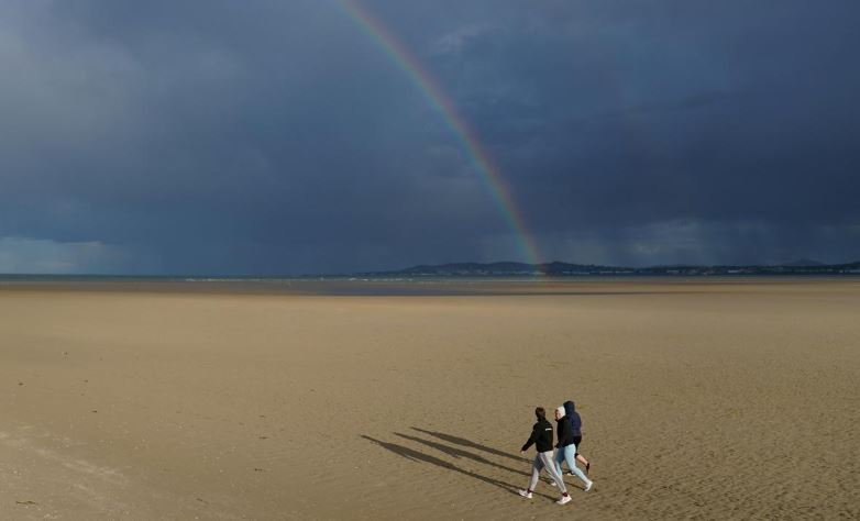  A rainbow and heavy rain are seen in the distance as people walk along an empty beach in sunshine, following the outbreak of the coronavirus disease (COVID-19), in Dublin, Ireland, June 5, 2020. File Photo: Reuters
