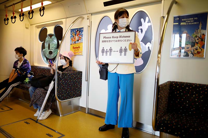 A staff member holds a sign to remind visitors to practice social distancing before the reopening of Tokyo Disneyland along with Tokyo DisneySea, which closed for months due to the coronavirus disease (COVID-19) outbreak, at a Disney Resort line train in Urayasu, east of Tokyo, Japan, on July 1, 2020. Photo: reuters
