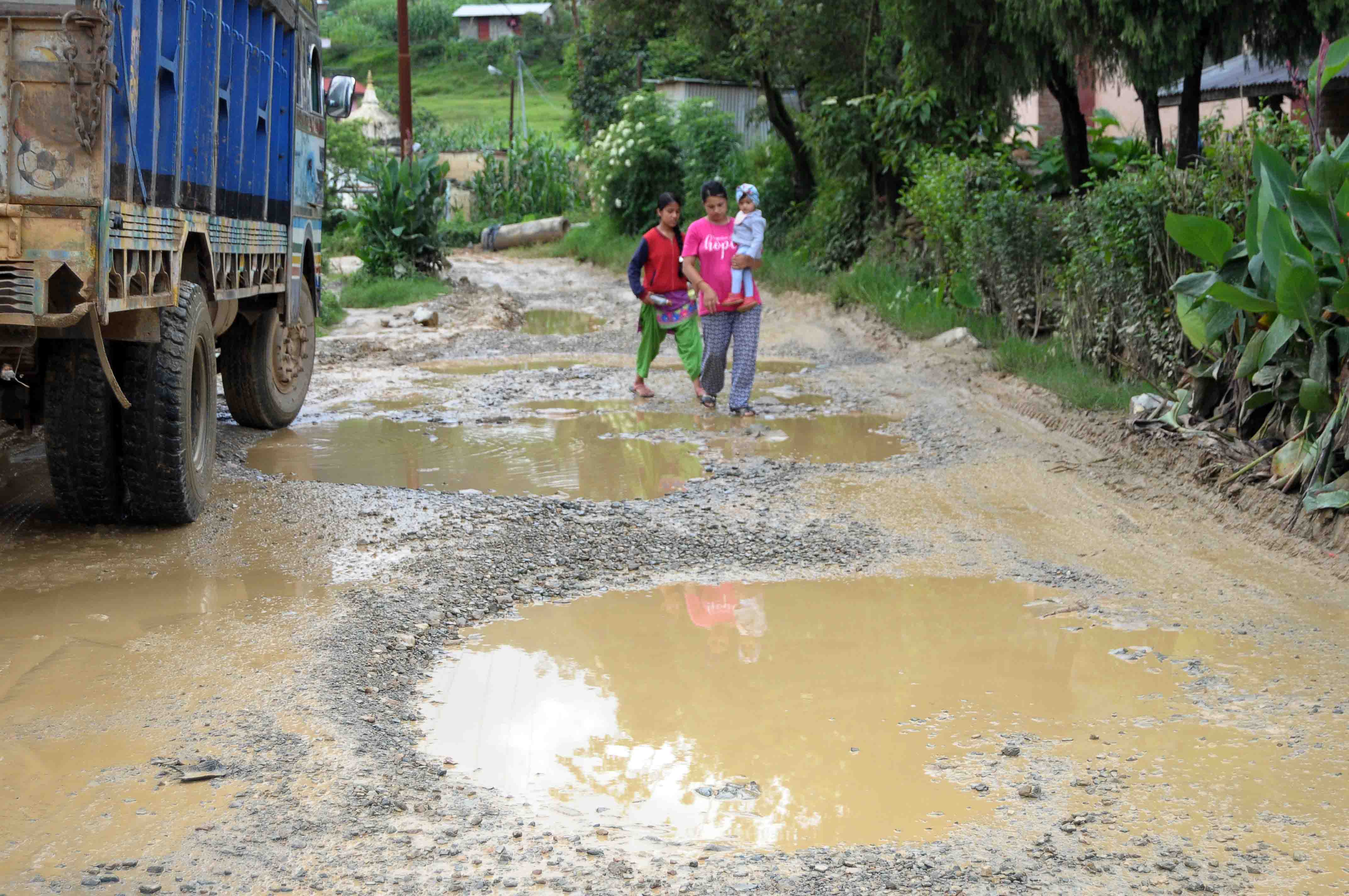 A woman carries a baby as she navigates along the puddle while a vehicle passes by along the Tikabhairav-Lele road section, in Lalitpur, on Tuesday, July 07, 2020. Photo: Balkrishna Thapa Chhetri/THT