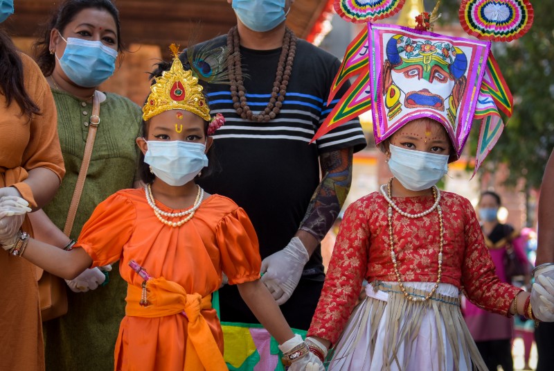 Kids dressed in various costumes and people holding the portraits of their departed loved ones participate in a procession during Gai Jatra festival, at Hanumandhoka, in Kathmandu, on Tuesday, August 4, 2020. They are wearing masks and face shields as they observe the festival amid COVID-19 pandemic. Photo: Naresh Shrestha/THT