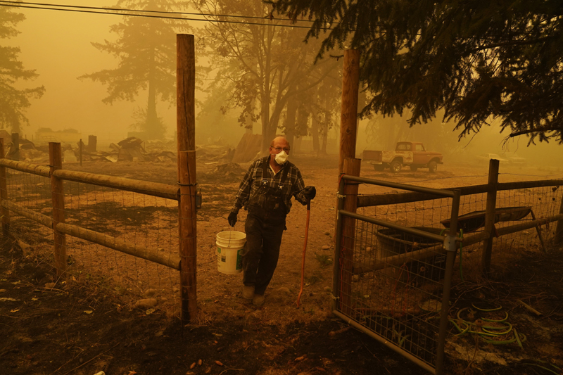 George Coble carries a bucket of water to put out a tree still smoldering on his property destroyed by a wildfire Saturday, Sept. 12, 2020, in Mill City, Ore. Photo: AP