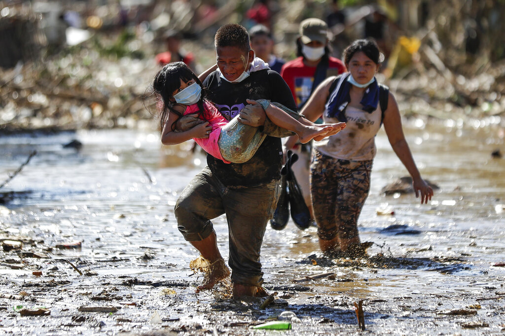 A man carries a girl through debris and floods in the typhoon-damaged Kasiglahan village in Rodriguez, Rizal province, Philippines on Friday, Nov. 13, 2020. Thick mud and debris coated many villages around the Philippine capital Friday after Typhoon Vamco caused extensive flooding that sent residents fleeing to their roofs and killing dozens of people. Photo: AP