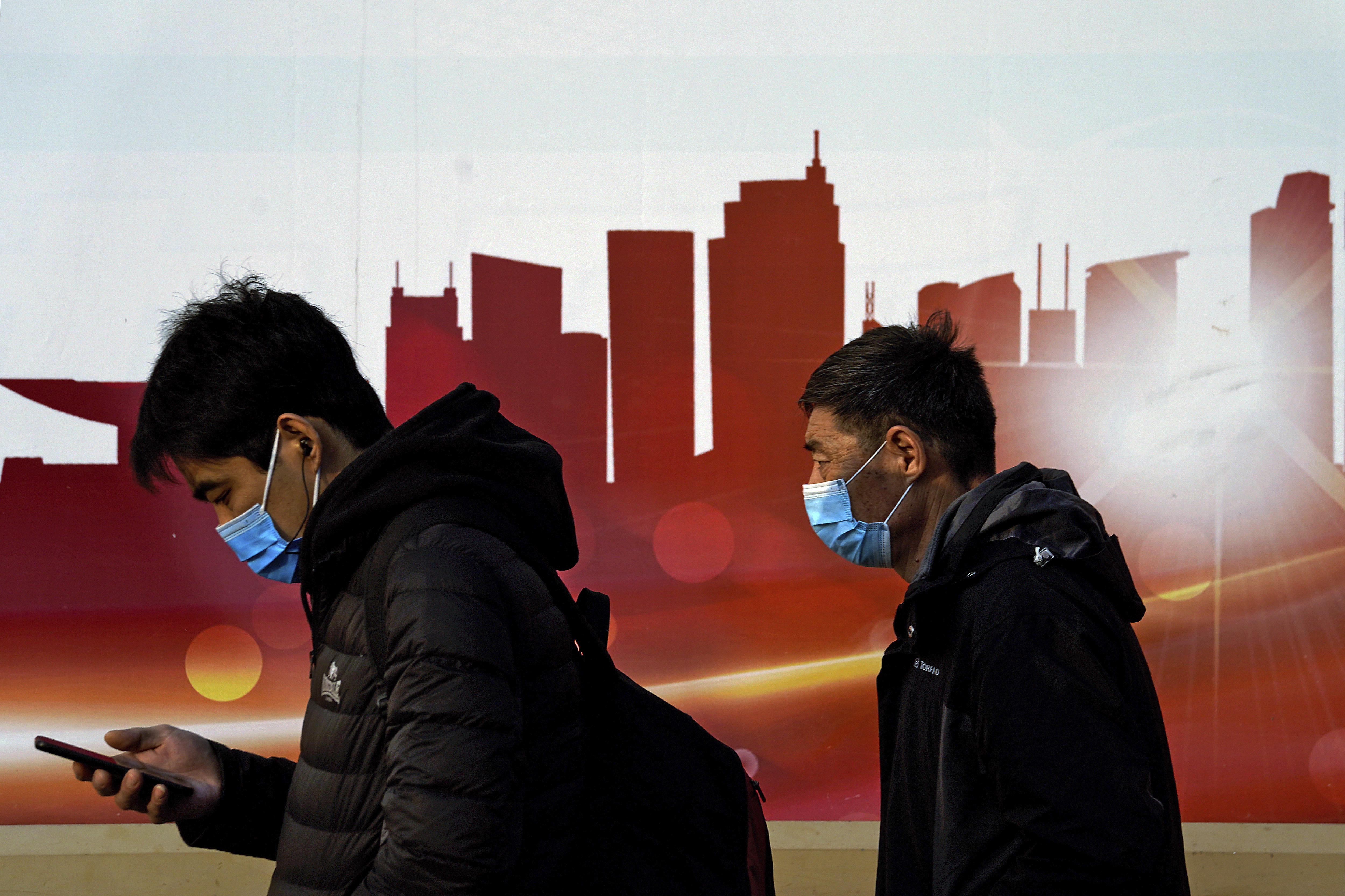 People wearing face masks to help curb the spread of the coronavirus walk by a moral depicting China's skyscrapers along a street in Beijing, Sunday, Dec. 6, 2020. Provincial governments across China are placing orders for experimental, domestically made coronavirus vaccines, though health officials have yet to say how well they work or how they may reach the country's 1.4 billion people. Photo: AP